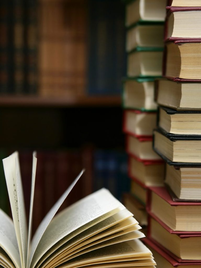 An open book in front of two piles of books.